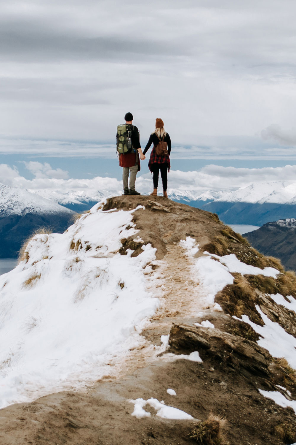 Photo of two people holding hands, standing on top of a mountain